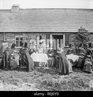 Alate Victorian vintage photographie noir et blanc, montrant un groupe de femmes habillées en costume traditionnel gallois, en dehors d'une petite maison. Certains boivent le thé, certains font de la couture. Le chapeau traditionnel Gallois est très bien illustré. Banque D'Images