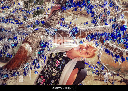 Jeune fille près de vieil arbre décoré avec le blue-eyes - amulettes Nazars, faite de verre bleu. Protéger contre le mauvais œil en parc national de Göreme, Cappadoci Banque D'Images