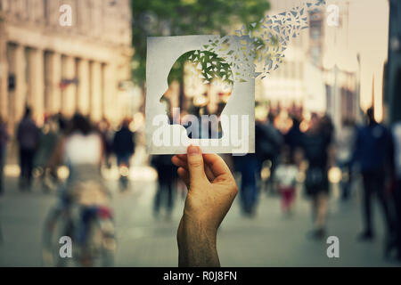 Main tenant une feuille de papier avec les droits de l'icône de la tête en morceaux sur une rue bondée de fond. Concept de la perte de mémoire et la démence de la maladie. Alzh Banque D'Images