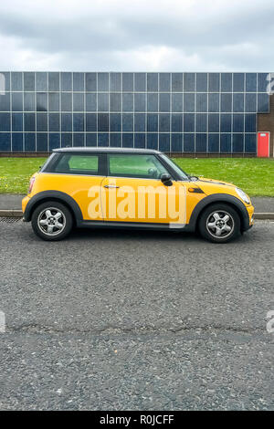 BMW Mini jaune voiture 3 portes avec un toit noir contrastant garé sur le côté de la route en face d'un bâtiment recouvert de panneaux solaires Banque D'Images