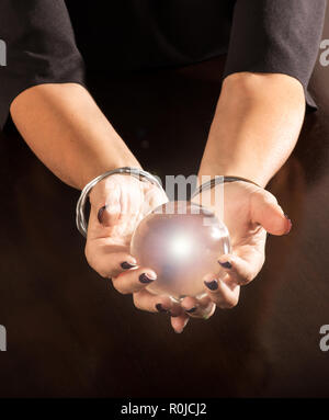 Fortune Teller tenant une boule de cristal brillant magique bercé dans ses mains sur une table sombre avec copie espace ci-dessous Banque D'Images