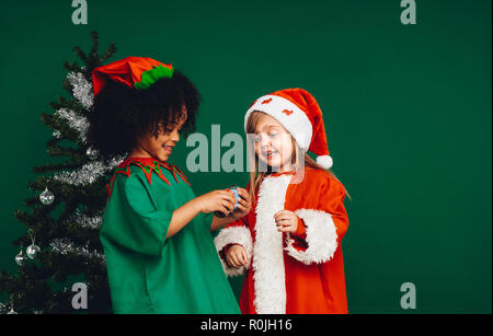 Enfants heureux en jouant avec leurs costumes de Noël cadeaux de Noël. Enfants multiethnique à un jouet à debout à côté d'un arbre de Noël décoré. Banque D'Images