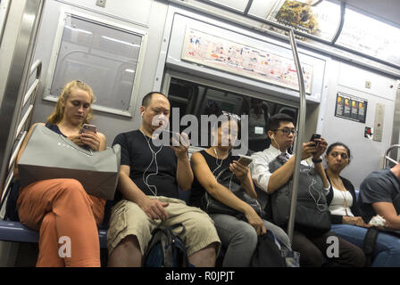 Utiliser leurs smartphones constamment les cavaliers et autres appareils électroniques tout en montant les wagons du métro de New York City. Banque D'Images