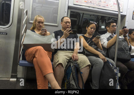 Utiliser leurs smartphones constamment les cavaliers et autres appareils électroniques tout en montant les wagons du métro de New York City. Banque D'Images