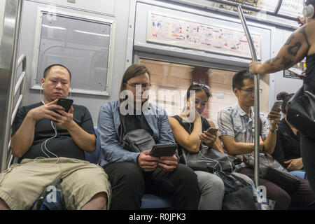 Utiliser leurs smartphones constamment les cavaliers et autres appareils électroniques tout en montant les wagons du métro de New York City. Banque D'Images