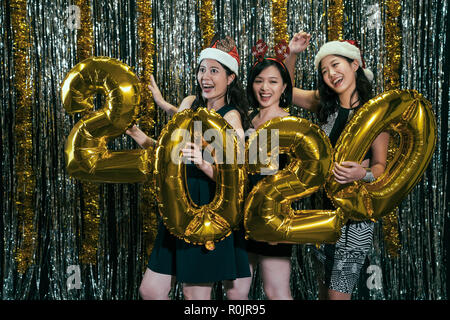 Des dames asiatiques s'amusant de l'or 2020 balloon danser dans une discothèque. cheerful young girls cill out celebrating new year eve avec santa vêtements. pa Banque D'Images