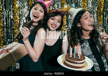 Amis heureux anniversaire à night club. jeunes femmes holding gift et gâteaux s'amusant dans un pub. les filles avec des chapeaux profitez d'événements célébrant les alcools. Banque D'Images