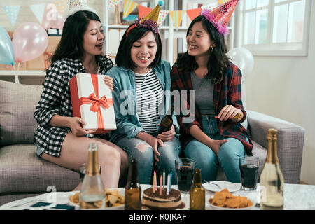 Groupe de jeunes amis avec des gâteaux et des bouteilles de verre celebrating birthday dans home intérieur. Soeur envoi boîte-cadeau pour surpris. belles filles en Banque D'Images