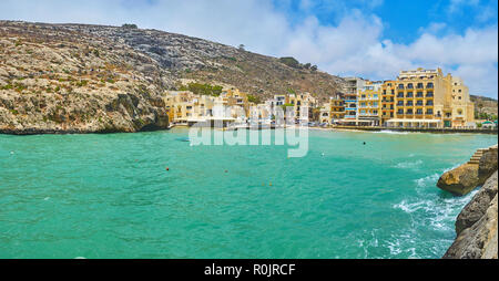 Le village de Xlendi port étroit avec des bateaux, posés sur les ondes de tempête, les hôtels modernes et des restaurants, face à la mer et les montagnes rocheuses autour de la Banque D'Images