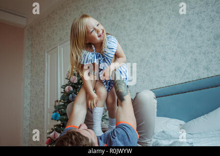 Papa jouant avec petite fille sur le lit chez lui Banque D'Images