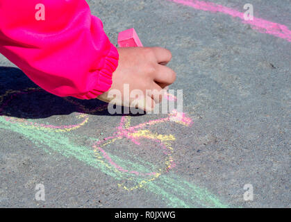 La main de l'enfant attire avec de la craie sur l'asphalte Banque D'Images