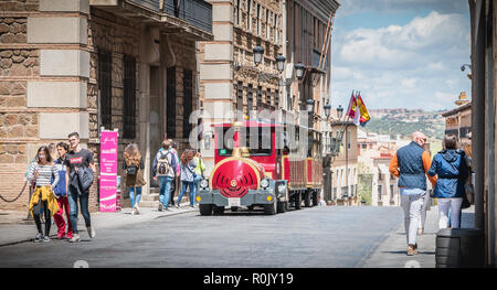 Tolède, Espagne - 28 Avril 2018 : promenade touristique dans une rue du quartier historique à côté d'un petit train rouge un jour de printemps Banque D'Images