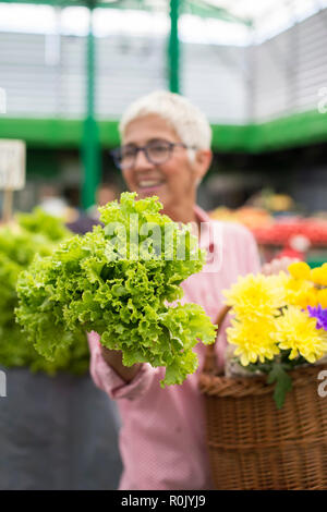 Portrait of senior woman détient panier de fleurs et achète sur le marché de la laitue Banque D'Images