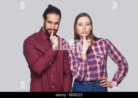 Portrait d'homme barbu et une femme sérieuse dans un style décontracté et permanent à la caméra à avec les doigts sur les lèvres et montrant le silence signe. Piscine studio s Banque D'Images