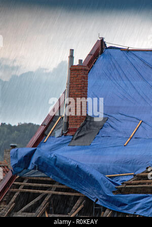 La bâche de protection sur le toit s'agite à la tempête avec pluie. La toile couvre le toit de la vieille maison à la reconstruction. Banque D'Images