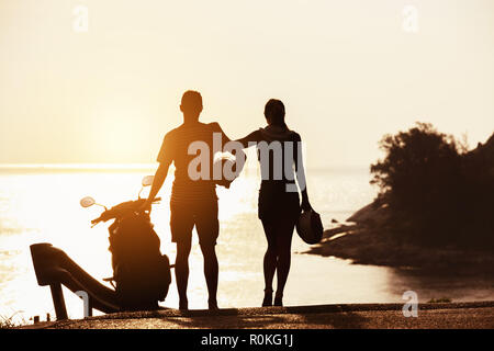 Les peuplements avec des silhouettes du couple contre moto coucher du soleil mer baie Banque D'Images