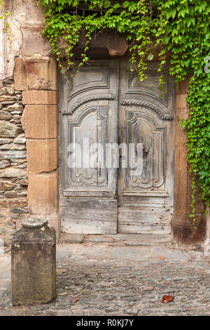 Vieille porte en bois, avec un couvert de lierre en pierre orné de pierres et de cailloux surround Banque D'Images
