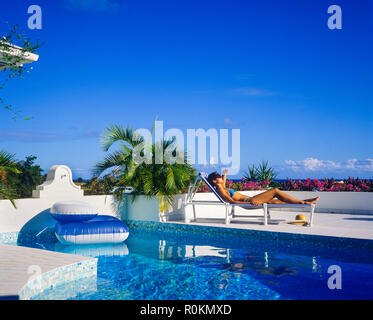 Jeune femme avec bikini bleu à bronzer sur une chaise longue au bord de la piscine, piscine, Guadeloupe, French West Indies, Banque D'Images