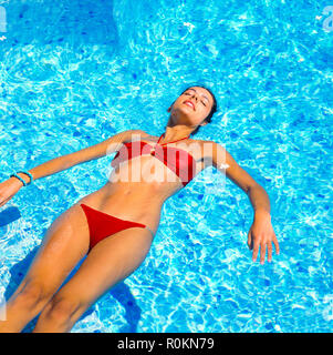 Jeune femme avec bandeau rouge flottant sur l'eau dans la piscine, Guadeloupe, French West Indies, Banque D'Images