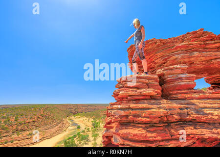 Backpaker femme de plus Nature's iconic Fenêtre, avec des roches a ondulé en rouge et blanc bagué, pointant Murchison River dans le Parc National de Kalbarri, dans l'ouest de l'Australie. L'Australie, l'outback voyage. Copier l'espace. Banque D'Images