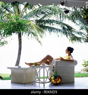 Jeune femme se détendre dans un fauteuil en rotin blanc, terrasse, jardin tropical, palmier, Guadeloupe, French West Indies, Banque D'Images