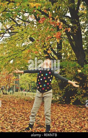 9 ans caucasien enfant, fille, heureux dans le parc, dresser des feuilles d'automne séchées au-dessus d'elle. La verticale Banque D'Images