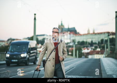 Mature businessman with suitcase marcher sur un pont de la ville de Prague. Banque D'Images