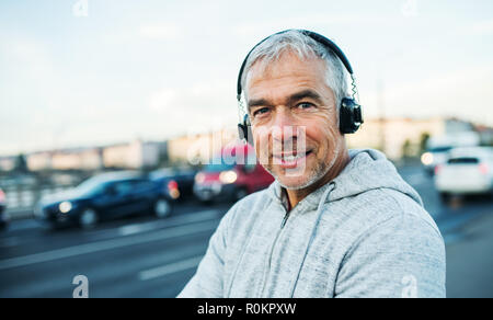 Mâle mature runner avec un casque à l'extérieur en ville, écouter de la musique. Banque D'Images