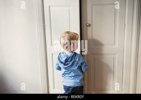 Une vue arrière du tout-petit garçon debout près de la porte à l'intérieur dans une chambre à coucher. Banque D'Images