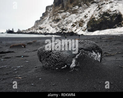 2 personnes marchant sur la plage près de Reynisdranga noir volcanique en Islande. Les roches du premier plan donne une perspective étrange au ballast rock derrière Banque D'Images