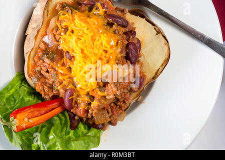 Pomme de terre cuite au four avec une veste de viande hachée surmontée de remplissage de chili avec du fromage râpé. Banque D'Images