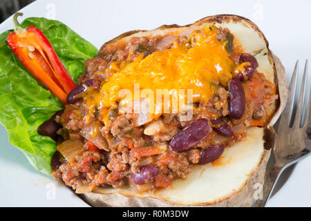 Pomme de terre cuite au four avec une veste de viande hachée surmontée de remplissage de chili avec du fromage râpé. Banque D'Images