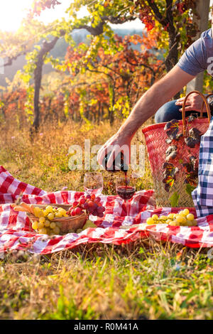 Pique-nique au coucher du soleil dans les collines de l'Italie. Les vignes et la nature ouverte à l'automne. Dîner romantique, un homme se verse un verre de vin rouge. Espace libre pour le texte. Copier l'espace. Banque D'Images