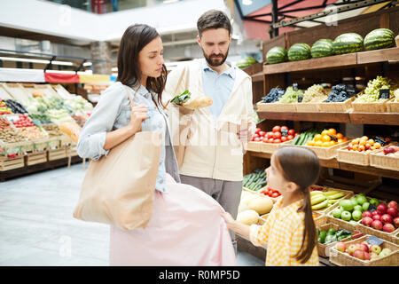 Petite fille jupe mères tirant tout en demandant d'acheter quelque chose dans un magasin d'alimentation au sérieux, les parents à l'écoute de sa demande Banque D'Images