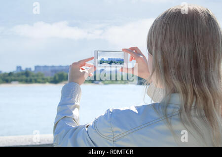 Une fille sur le bord de l'eau prend des photos sur un smartphone. Banque D'Images