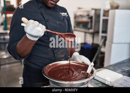 Travailleur ayant une cuillère pleine de chocolat fondu artisanale Banque D'Images