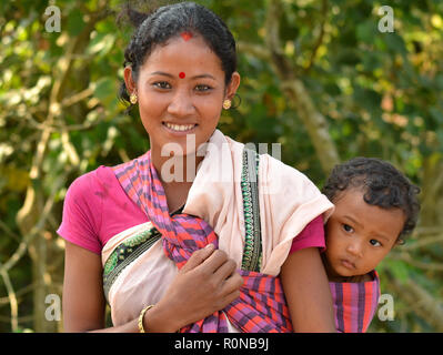 Les jeunes du nord-est de l'Inde tribale Mishing femme de l'Île Majuli porte son bébé curieux garçon dans une écharpe porte-bébé sur son dos. Banque D'Images