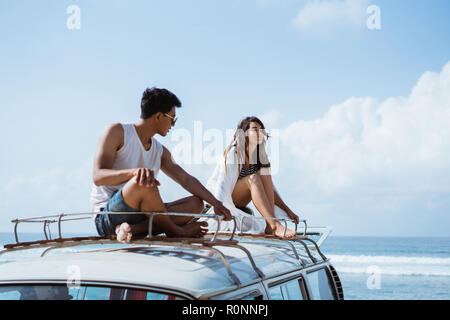 Jeune couple avec des lunettes de soleil assis sur le dessus de toit minifourgonnette Banque D'Images