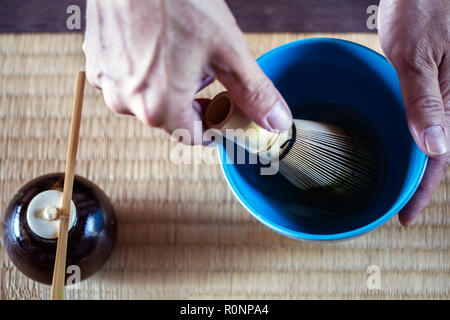 High angle portrait de personne à l'aide d'un fouet en bambou pour préparer le thé Matcha dans un bol bleu au cours de cérémonie du thé. Banque D'Images