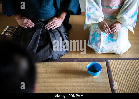 Portrait de l'homme et de la femme japonaise traditionnelle portant des kimono blanc avec motif floral bleu à genoux sur le plancher pendant la cérémonie du thé, holding blu Banque D'Images