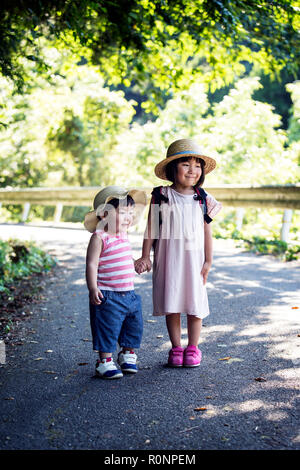 Deux filles japonaises portant des chapeaux soleil debout sur chemin, se tenant la main. Banque D'Images