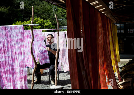 L'homme japonais assis à l'extérieur une usine textile atelier de teinture, de raccrocher de rose fraîchement tissu. Banque D'Images