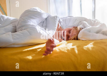 Garçon couché au lit dormir dans la lumière du matin Banque D'Images