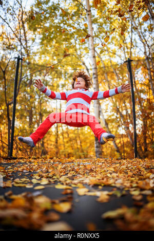 Garçon sautant sur un trampoline recouvert de feuilles d'automne, United States Banque D'Images