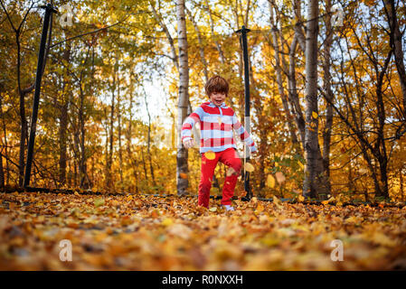 Garçon debout sur un trampoline recouvert de feuilles d'automne, United States Banque D'Images