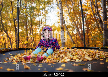 Smiling girl sitting on une pile de feuilles d'automne sur un trampoline, United States Banque D'Images