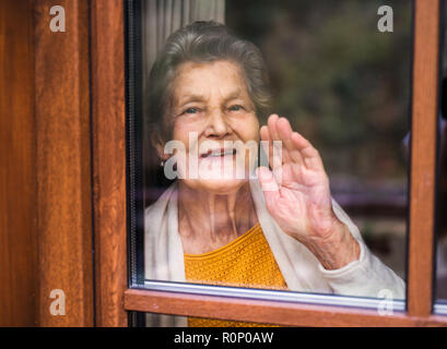 Une vieille femme debout près de la fenêtre, à l'extérieur. Tourné à travers le verre. Banque D'Images