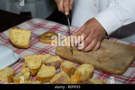 Gros plan d'une femme de couper le pain de pommes de terre traditionnelle de Santana, l'île de Madère, sur planche de bois. Banque D'Images