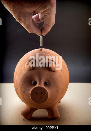 Part le fait de lancer une monnaie dans une tirelire de porcinet de boue, conceptual image Banque D'Images