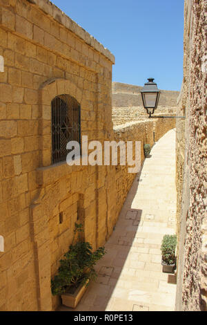 Vue de la chambre d'une fenêtre dans la vieille ville pour affiner l'ancienne rue vide jaune avec lanterne en journée ensoleillée sous le ciel bleu. Victoria, Gozo, Malte Banque D'Images